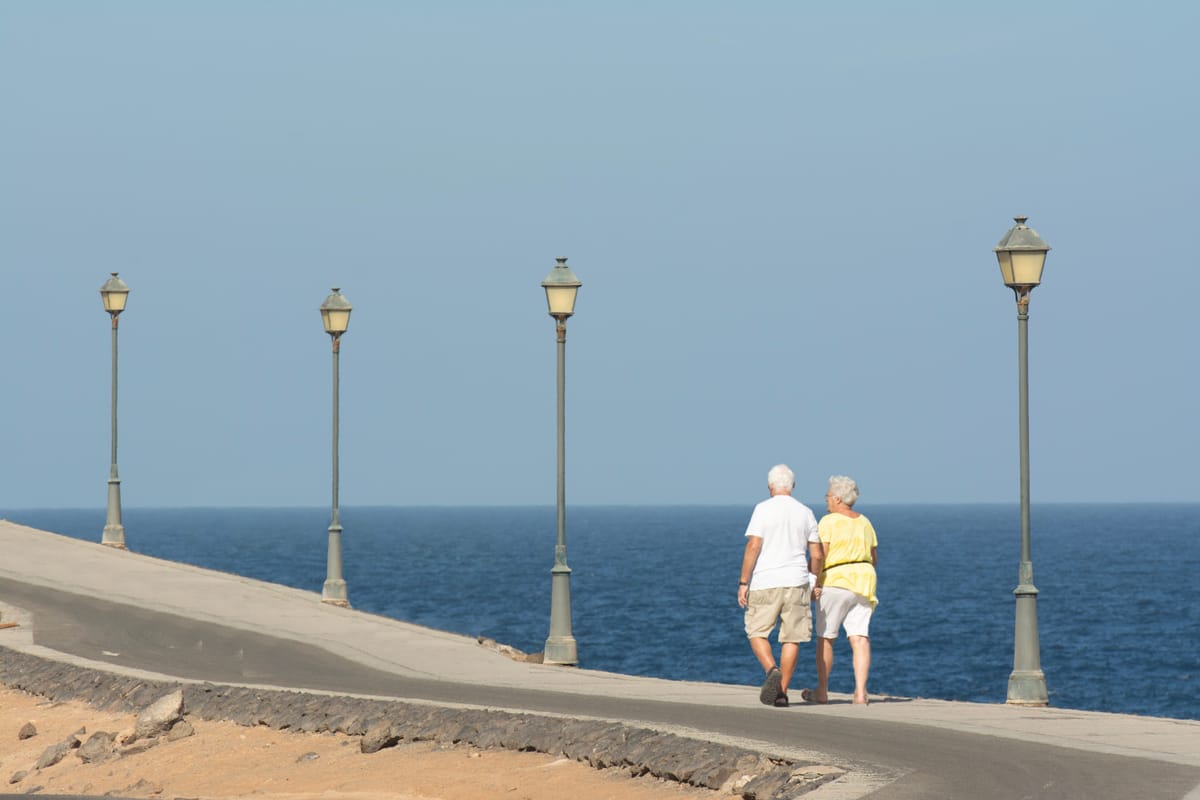 Et eldre par går tur langs en strandpromenade
